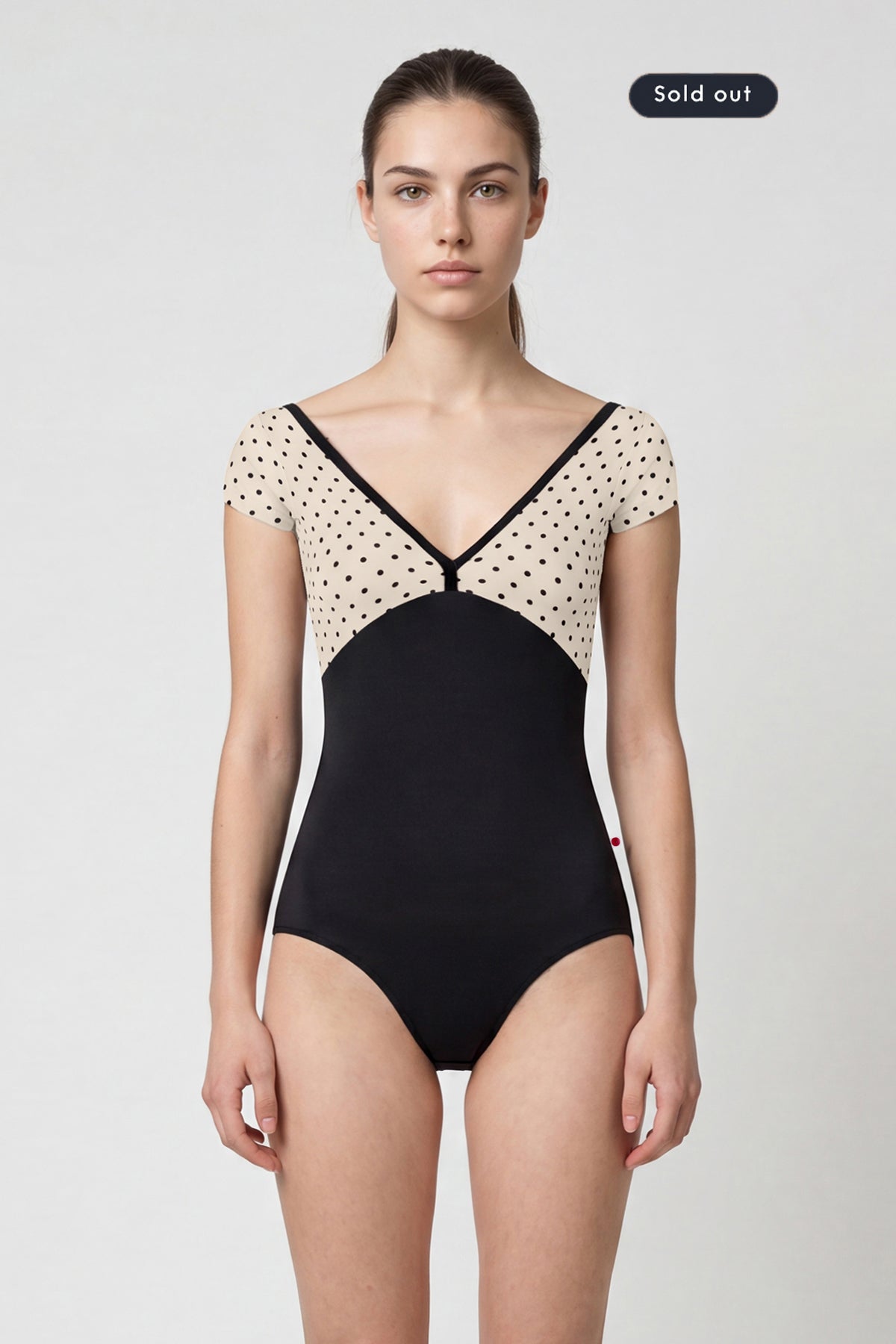 AI-generated model. Alicia leotard, cream polka-dot cap-sleeve bodice with black V-neck trim and black body.