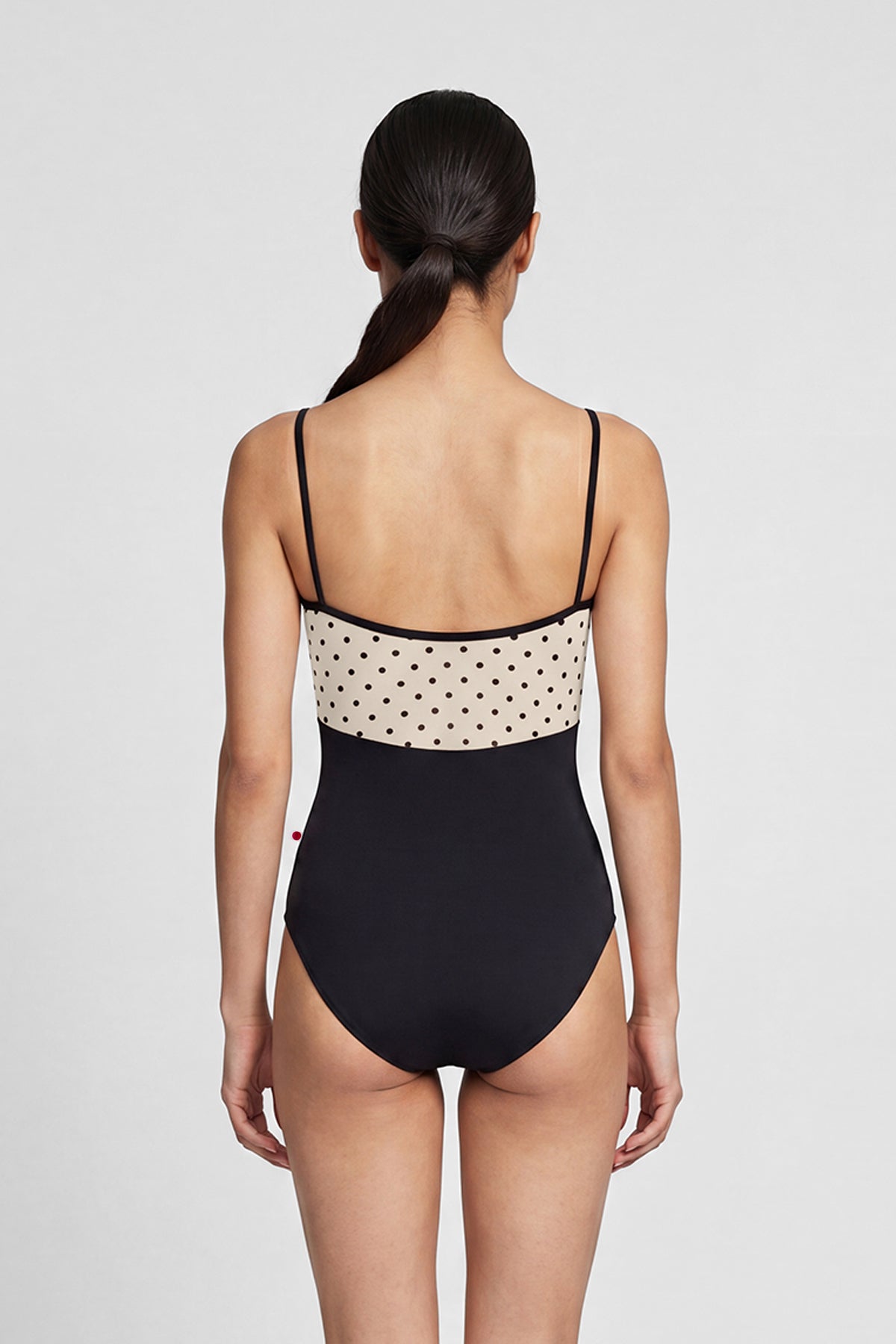 AI-generated model. Denise leotard, cream polka-dot bust panel and black body, straight neckline with thin black straps.
