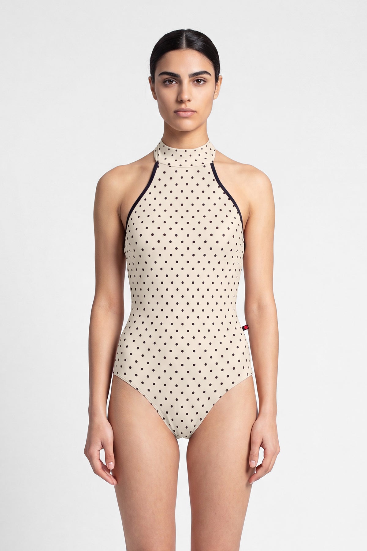AI-generated model. Kelly leotard, all-over T-Lunares Cream polka-dot with a black-trimmed high halter neck and open sides.