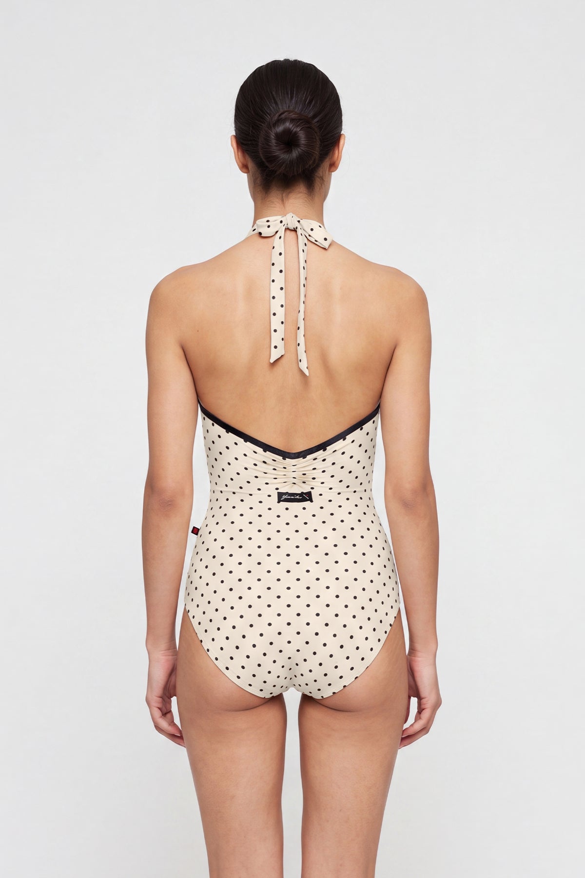 AI-generated model. Kelly leotard, all-over T-Lunares Cream polka-dot with a black-trimmed high halter neck and open sides.