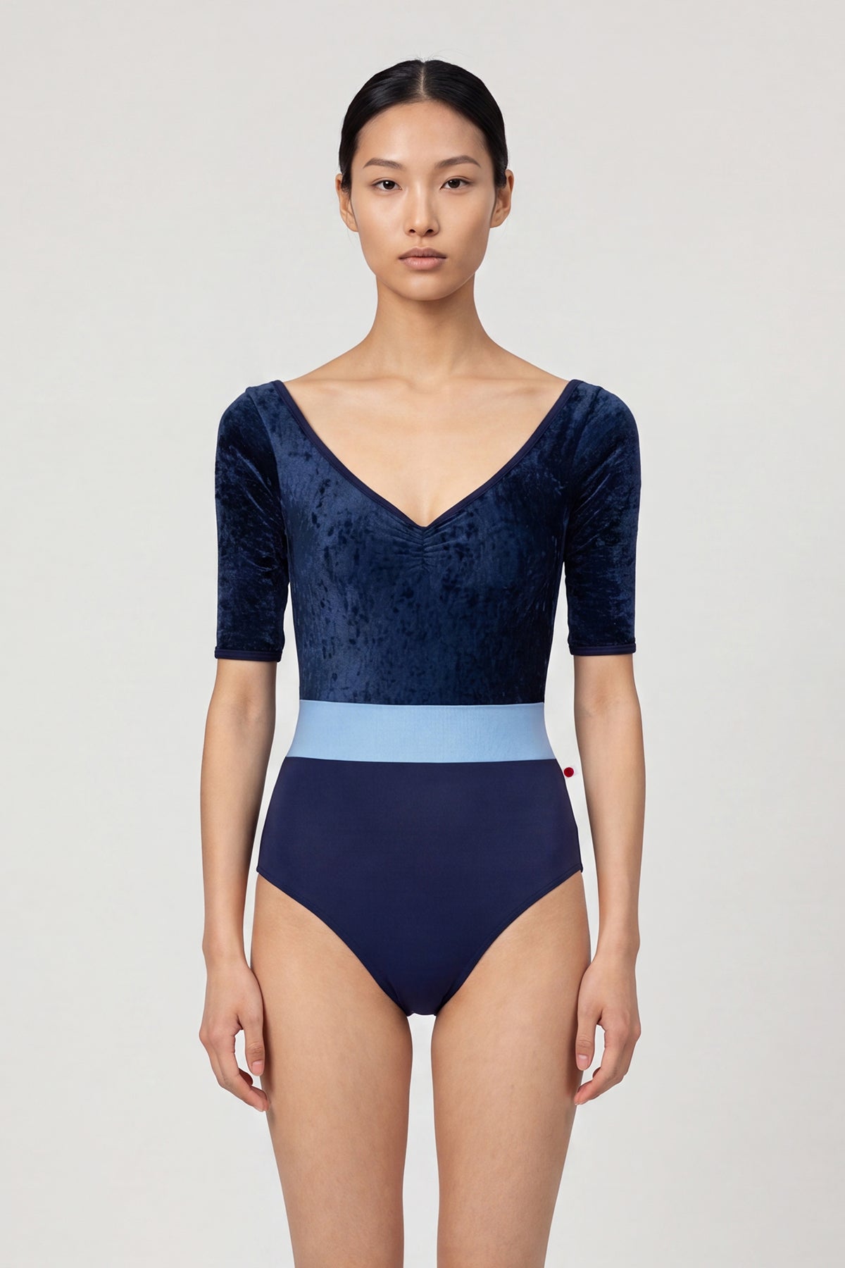 AI-generated model. Lucy leotard, navy crushed-velvet elbow-sleeve bodice with a light-blue waistband and a navy body, V-neck.