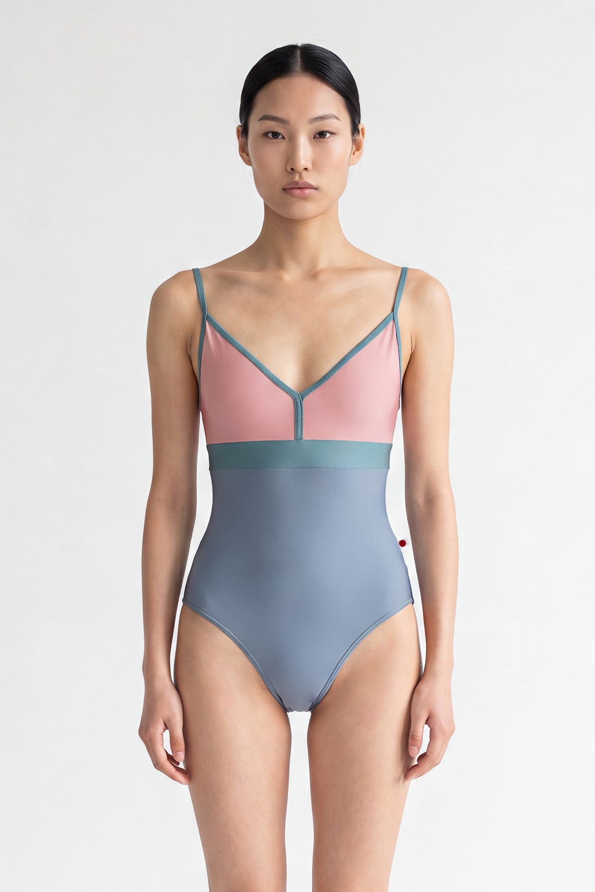 AI-generated model. Zoe leotard, dusty-rose bust and blue-grey body with a teal waistband and thin teal straps, V-neck.