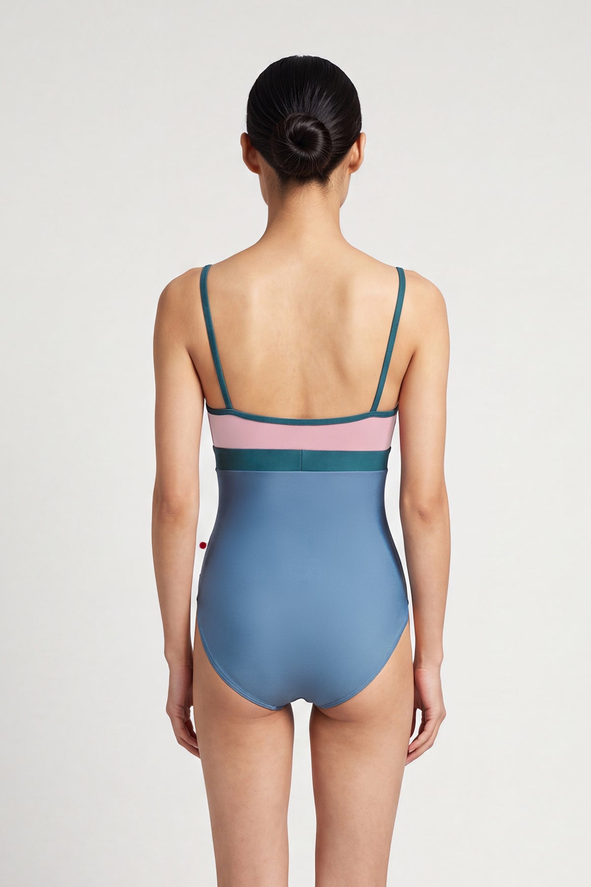 AI-generated model. Zoe leotard, dusty-rose bust and blue-grey body with a teal waistband and thin teal straps, V-neck.