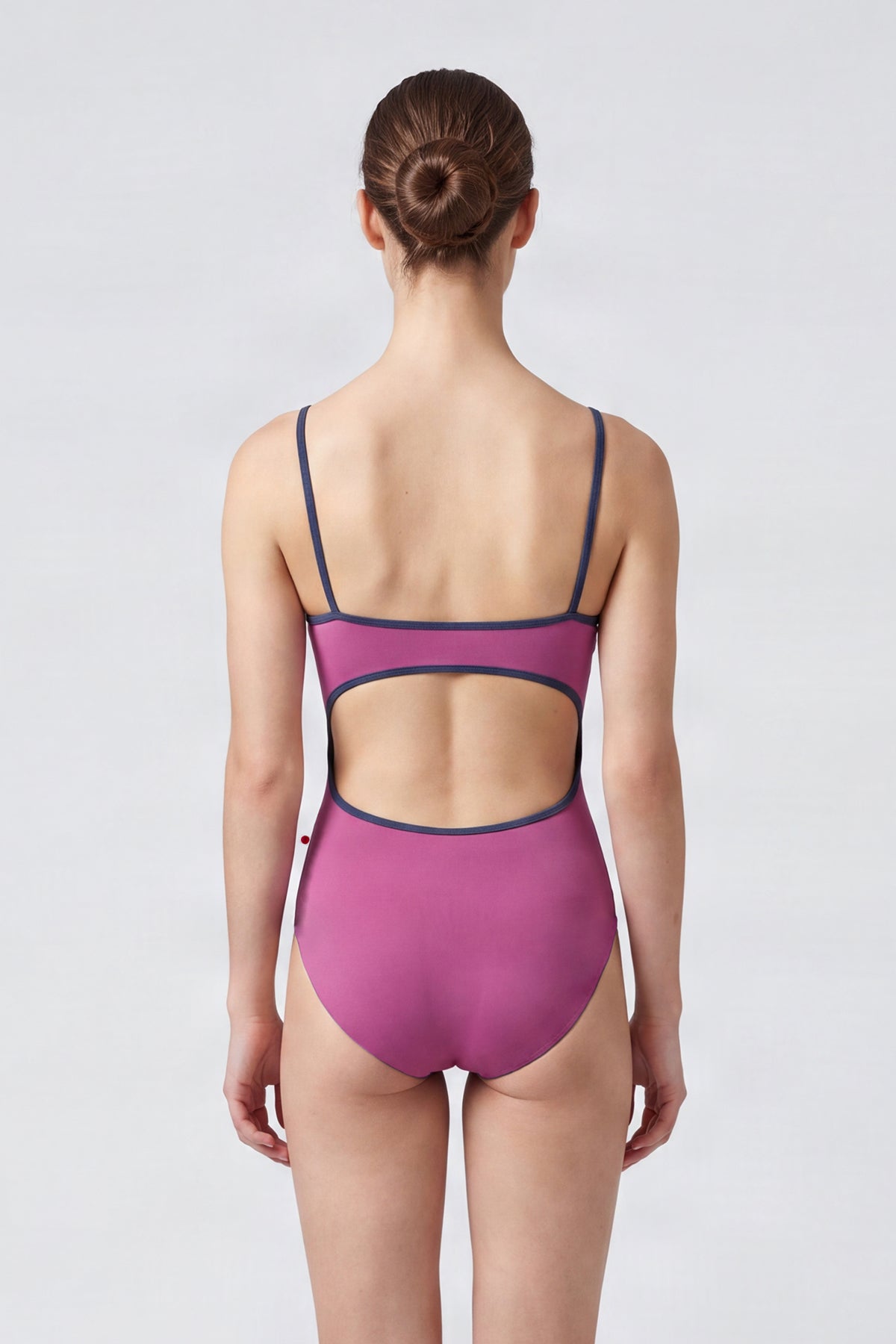 AI-generated model. Kiki leotard, orchid-pink with a scoop neck and charcoal strap trim.
